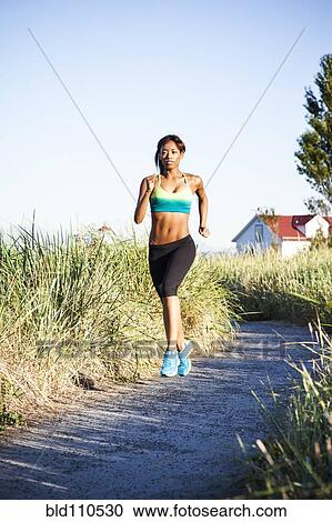 Stock Image - Mixed race woman running on dirt road. Fotosearch