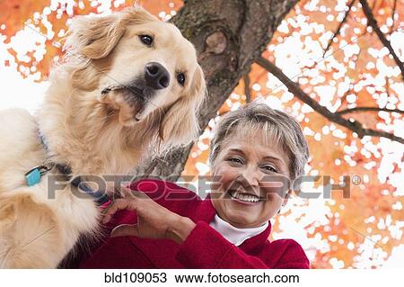Stock Image - Mixed race woman with dog in park. Fotosearch