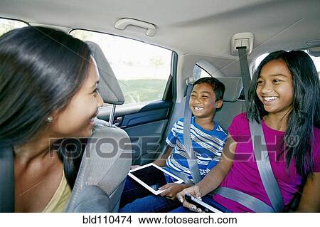 Picture - Mother watching children use technology in car. Fotosearch