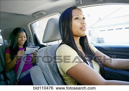 Stock Photograph - Mother watching daughter use technology in car. Fotosearch