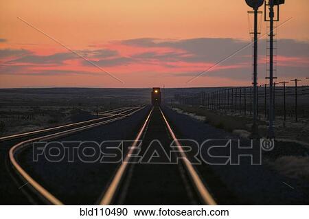 Stock Image - Sunset over train on tracks in rural landscape. Fotosearch
