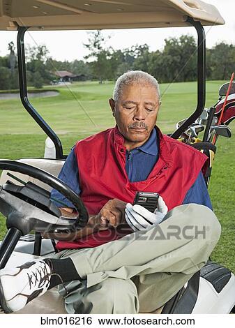 Stock Photograph - Black man using cell phone in golf cart. Fotosearch