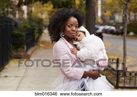 Stock Photograph - Black mother carrying daughter on city street. Fotosearch