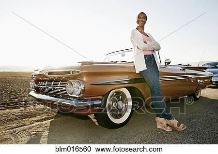 Stock Image - Black woman leaning on convertible. Fotosearch