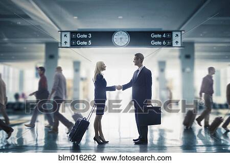 Stock Image - Business people shaking hands in airport. Fotosearch