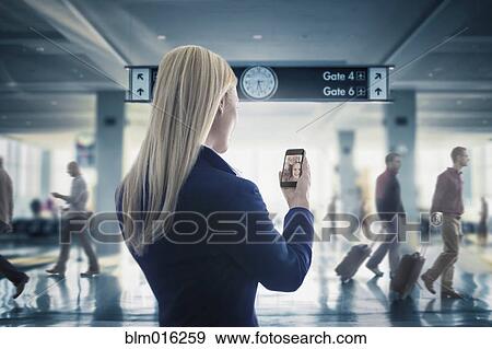 Stock Photo - Caucasian businesswoman text messaging on cell phone in airport. Fotosearch