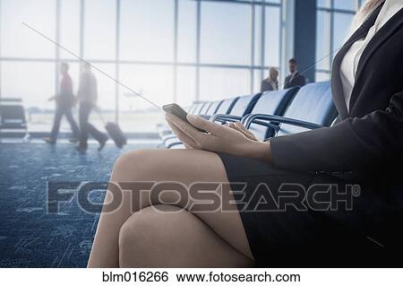 Stock Photograph - Caucasian businesswoman text messaging on cell phone in airport. Fotosearch
