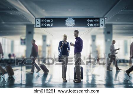 Stock Image - Caucasian couple looking at cell phone in airport. Fotosearch