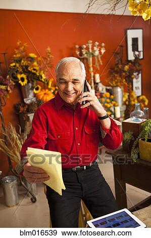 Stock Photo - Caucasian florist talking on phone in shop. Fotosearch