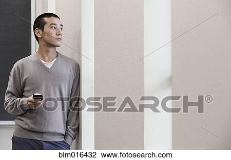Stock Image - Chinese man using cell phone in hallway. Fotosearch