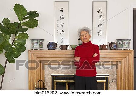 Stock Image - Chinese woman standing at fireplace. Fotosearch
