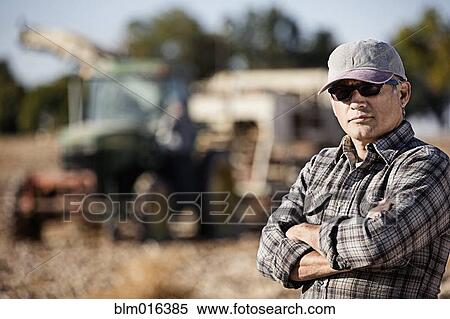 Stock Photography - Hispanic farmer standing by harvester. Fotosearch