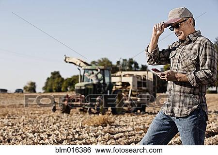 Stock Photograph - Hispanic farmer using cell phone in crop field. Fotosearch