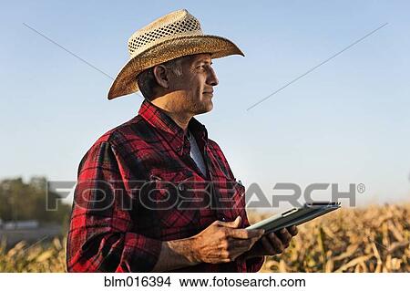 Picture - Hispanic farmer using tablet computer in crop field. Fotosearch