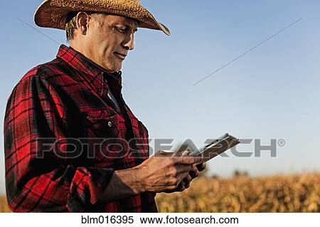 Stock Photography - Hispanic farmer using tablet computer in crop field. Fotosearch