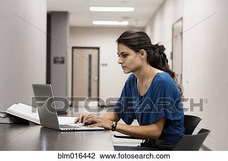 Stock Image - Hispanic student using laptop in hallway. Fotosearch