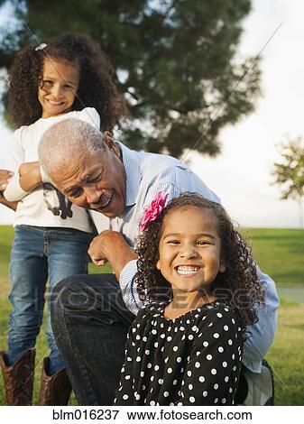 Stock Photo - Man playing with granddaughters outdoors. Fotosearch