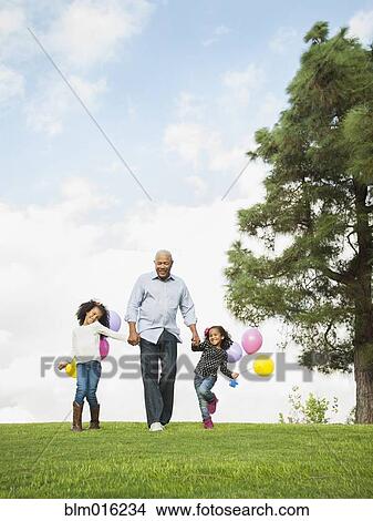 Picture - Man walking with granddaughters in park. Fotosearch
