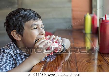 Stock Photo - Mixed race boy eating burger in restaurant. Fotosearch