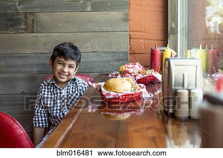 Stock Image - Mixed race boy having burgers in restaurant. Fotosearch