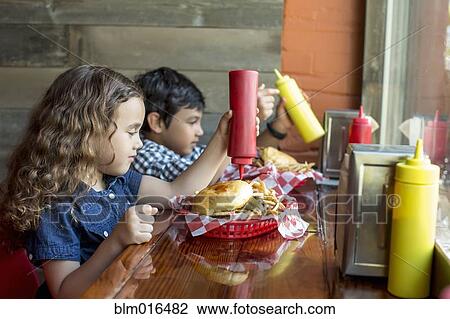 Stock Image - Mixed race children having burgers in restaurant. Fotosearch