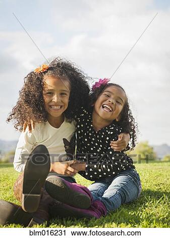 Stock Image - Mixed race girls sitting in grass. Fotosearch