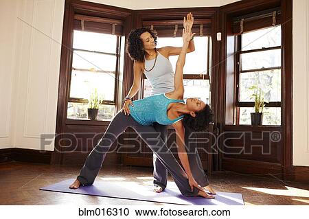 Stock Image - Mixed race women practicing yoga in living room. Fotosearch