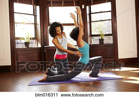 Stock Image - Mixed race women practicing yoga in living room. Fotosearch