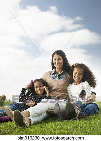 Stock Image - Mother and daughters sitting in grass. Fotosearch