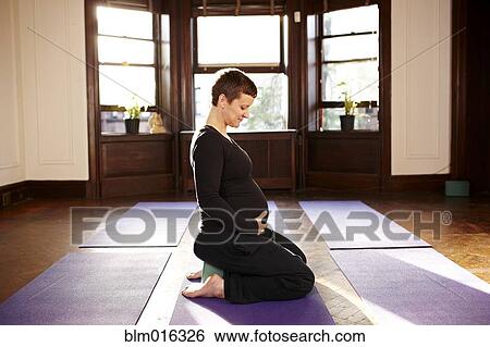 Stock Photograph - Pregnant woman sitting on yoga mat. Fotosearch