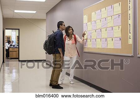 Stock Image - Students reading bulletin board in hallway. Fotosearch