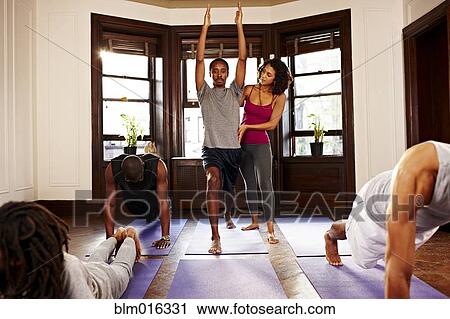 Stock Image - Teacher helping student in yoga class. Fotosearch