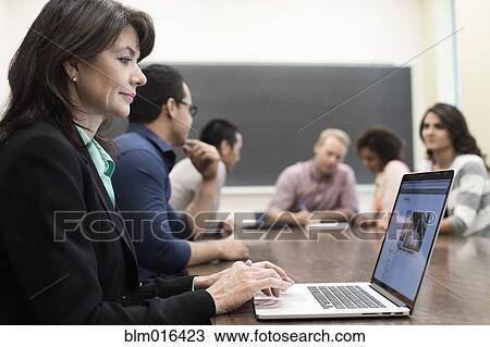 Stock Image - Teacher using laptop in classroom. Fotosearch