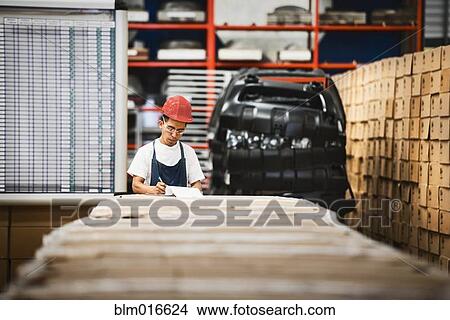 Picture - Worker examining product in manufacturing plant. Fotosearch