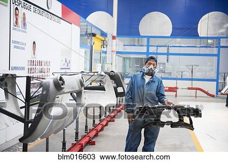 Stock Image - Worker holding machinery in manufacturing plant. Fotosearch