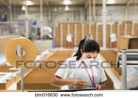Stock Image - Worker wearing face mask in manufacturing plant. Fotosearch