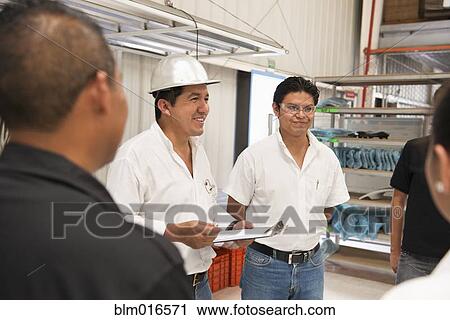 Stock Image - Workers talking in manufacturing plant. Fotosearch