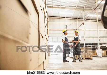 Stock Image - Workers talking in manufacturing plant. Fotosearch