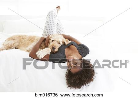 Stock Photograph - Black woman petting dog on bed. Fotosearch