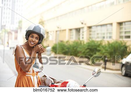 Stock Image - Black woman tying on helmet. Fotosearch