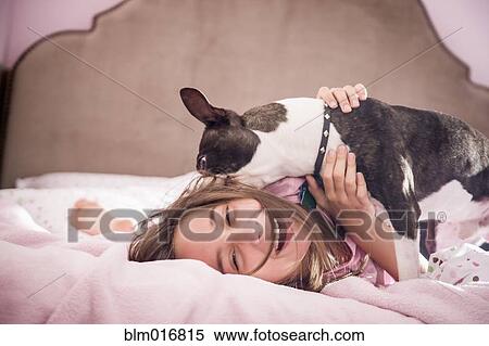 Stock Photography - Girl playing with dog on bed. Fotosearch
