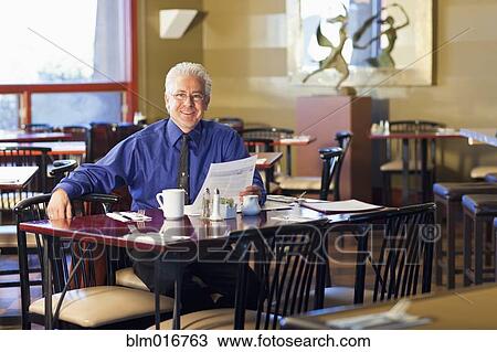 Stock Image - Hispanic cafe owner sitting at table. Fotosearch