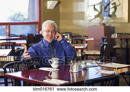 Stock Image - Hispanic cafe owner talking on cell phone. Fotosearch
