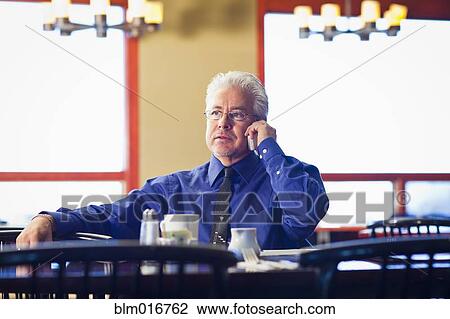 Stock Image - Hispanic cafe owner talking on cell phone. Fotosearch