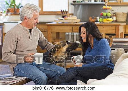 Stock Photograph - Hispanic couple petting dog in living room. Fotosearch