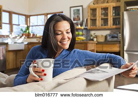 Stock Photo - Hispanic woman drinking coffee and reading newspaper. Fotosearch