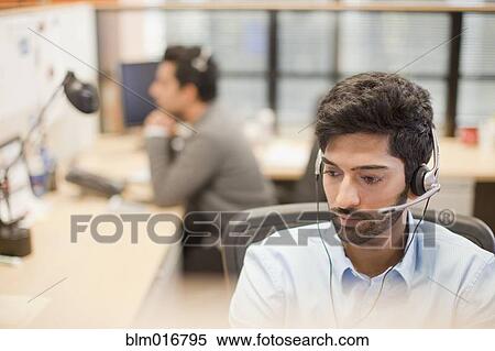 Stock Photography - Indian businessman wearing headset at desk. Fotosearch