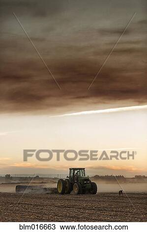 Stock Image - Tractor driving in crop field. Fotosearch