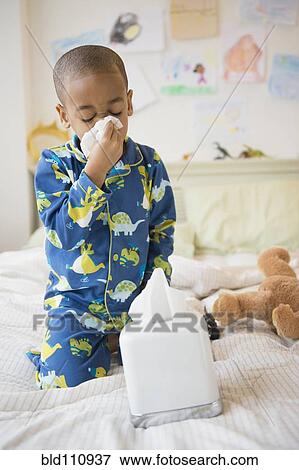 Stock Photo - African American boy blowing his nose on bed. Fotosearch