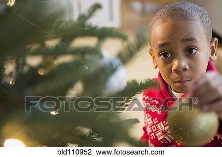 Stock Image - African American boy decorating Christmas tree. Fotosearch